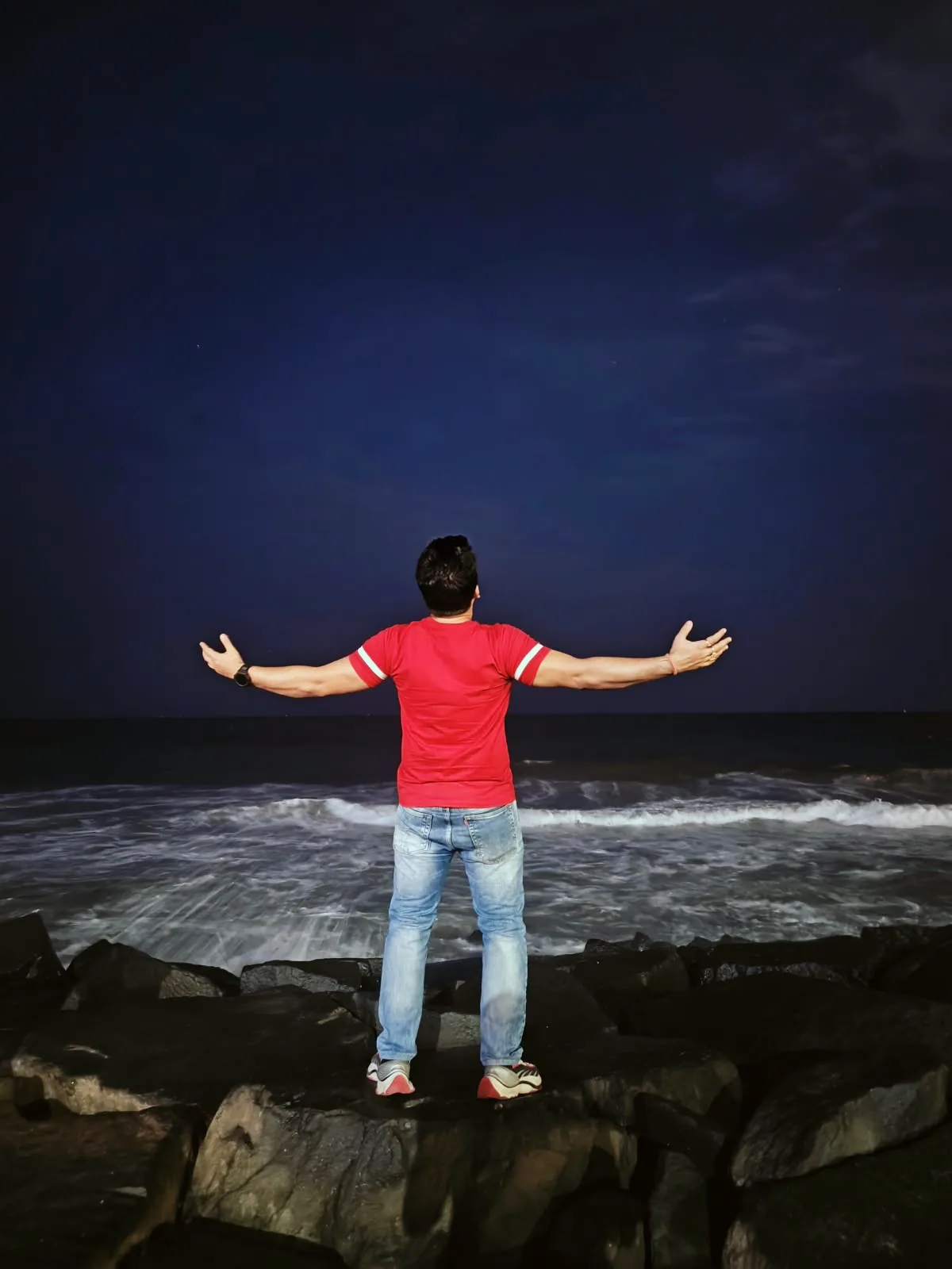 Gaurav standing at the edge of the sea with his arms open